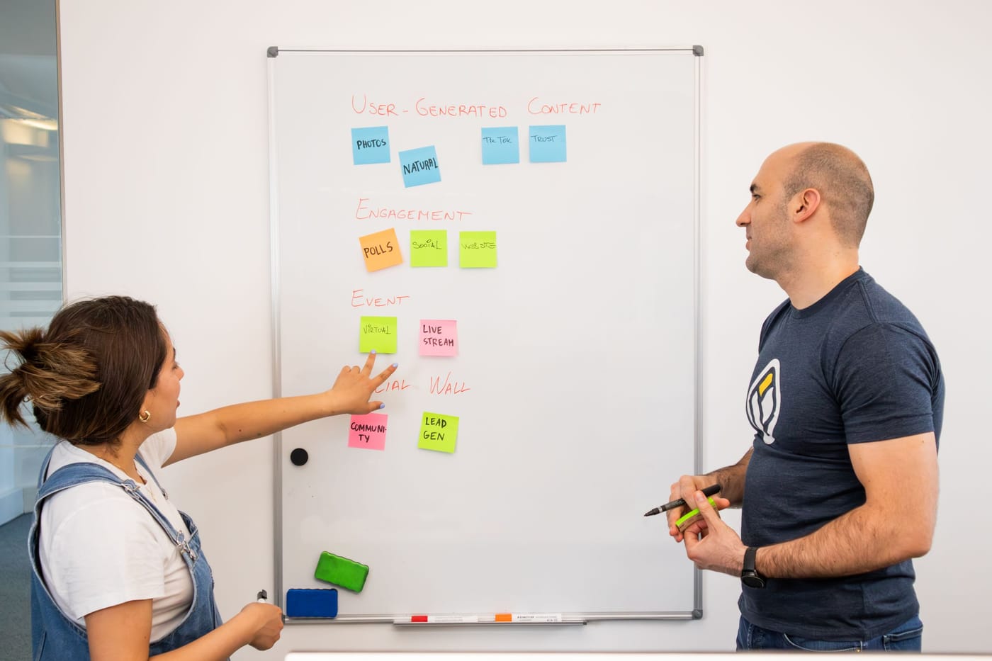 Two colleagues planning work on a whiteboard covered in sticky notes