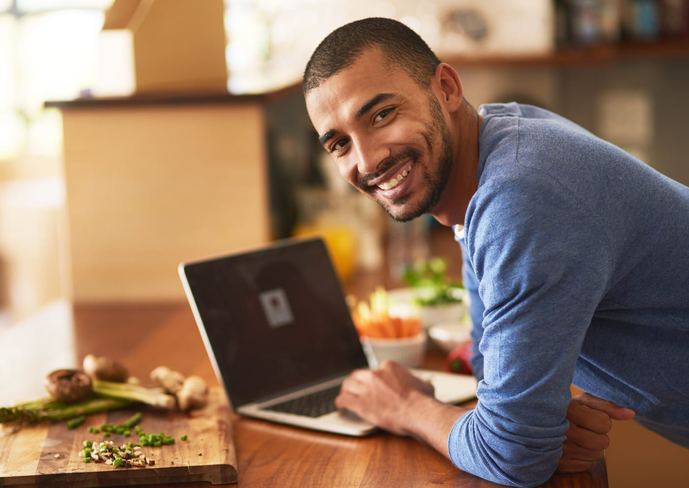 A smiling professional leaning over a laptop at a kitchen bench