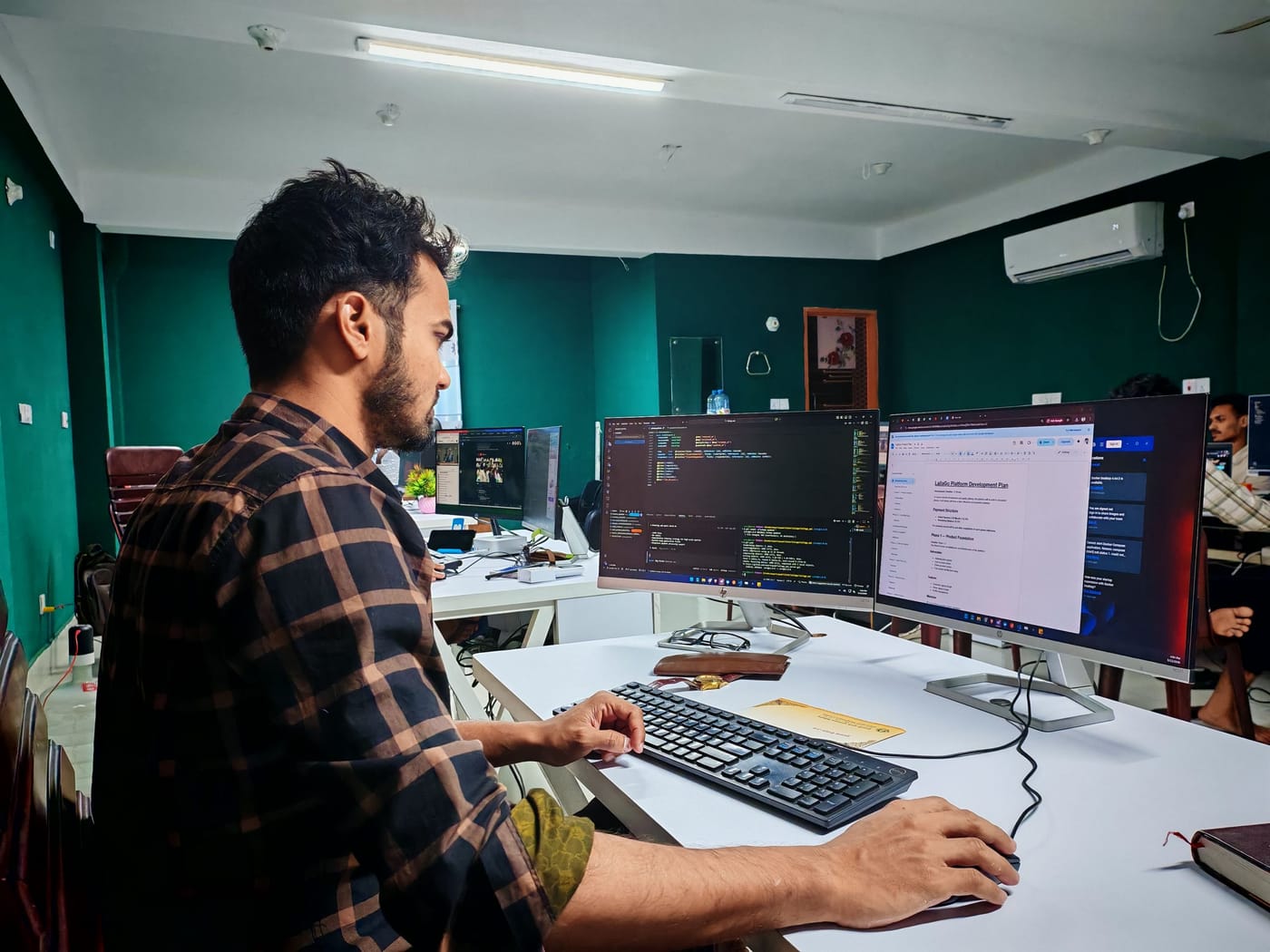 A software developer writing code across two monitors in a modern office