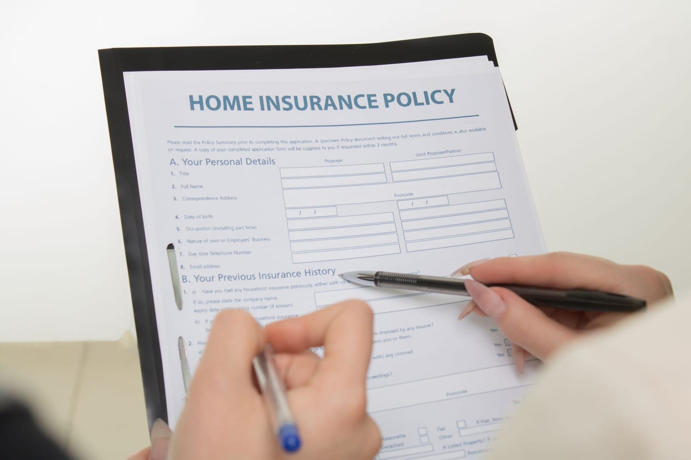 Hands signing a home insurance policy on a clipboard