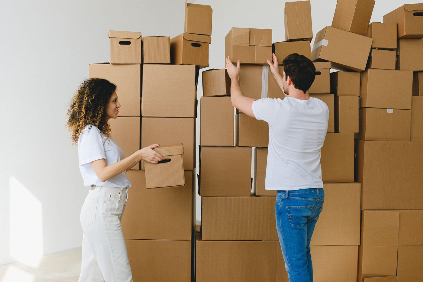 A couple stacking cardboard boxes in a new home after relocating