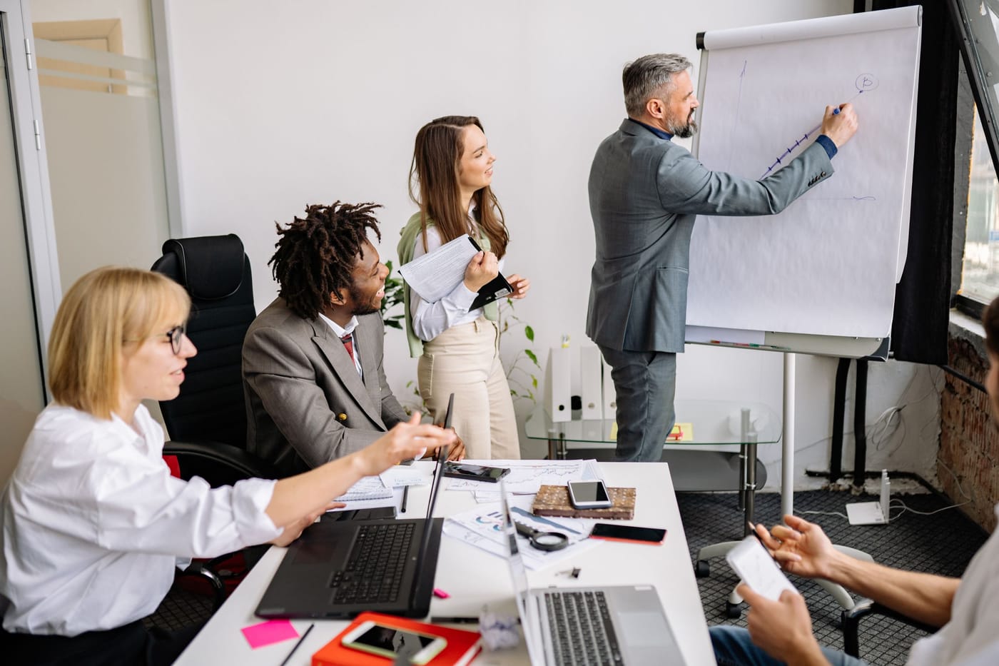 A consultant presenting at a flip chart to colleagues around a meeting table