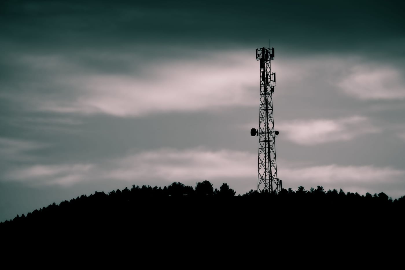 A telecommunications tower silhouetted against a dramatic sky
