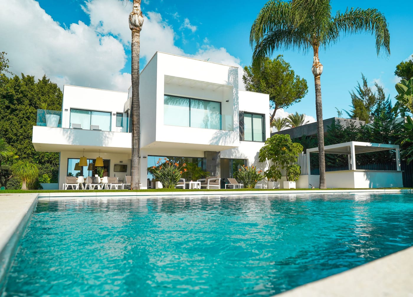 A modern white luxury villa with a swimming pool, palm trees and a sunlit garden